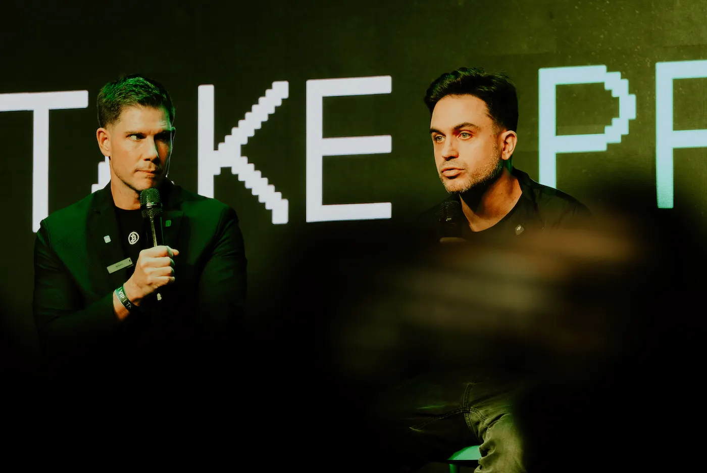 Dos speakers frente al logo Take Profit